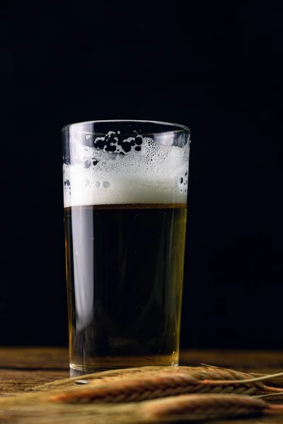 ライ麦の耳を持つ暗い背景に木製のテーブルの上に立って泡とビールのガラス — ストック写真