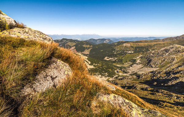 Горный пейзаж с камнями и травой на переднем плане
