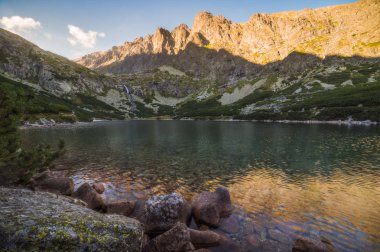 Gün batımında ön planda Rock ile dağ gölü