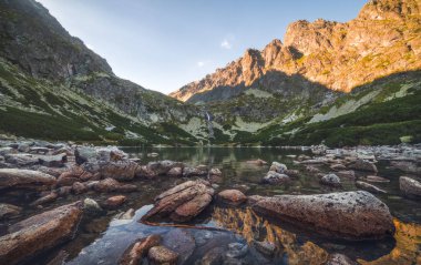 Gün batımında ön planda taşlarla dağ gölü
