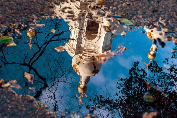 Ortodoks kilisesinin sonbaharda sudaki su birikintisindeki yansıması. Eski bir katedral, suyun içinde, bulanık. Mavi gökyüzü ve haç.