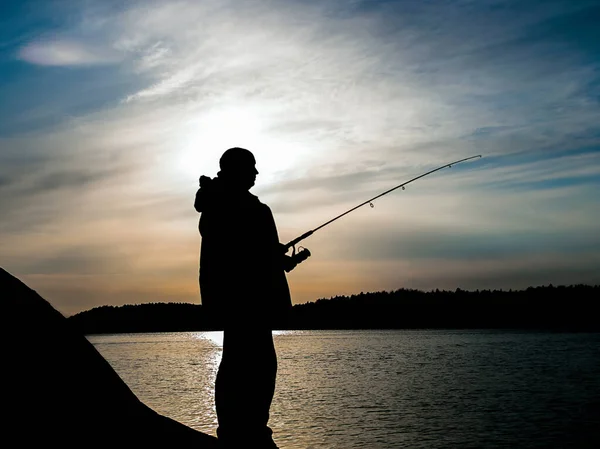 Pesca al atardecer en las Islas Aland en Finlandia. Silueta de un pescador con caña de pescar al atardecer. Luz trasera . — Foto de Stock