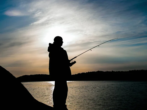 Angeln bei Sonnenuntergang auf den finnischen Inseln. Silhouette eines Fischers mit Angelrute im Sonnenuntergang. Gegenlicht. — Stockfoto