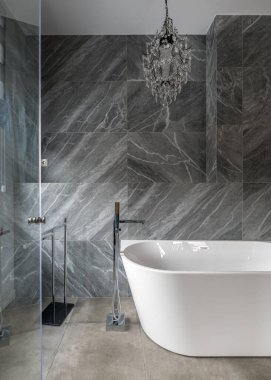 Doğal ışıkta mermer bir duvara yaslanmış kar beyazı küveti olan lüks bir banyo.