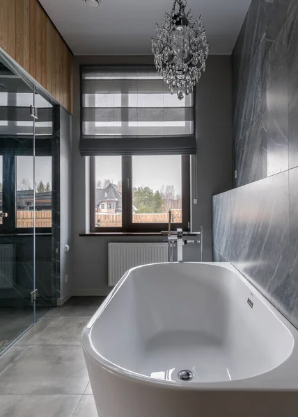 Doğal ışıkta mermer bir duvara yaslanmış kar beyazı küveti olan lüks bir banyo.