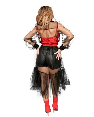 Beyaz arka planda seksi kahverengi saçlı bir manken, şık, şeffaf siyah bir elbise, deri şort ve kırmızı çizmeler..