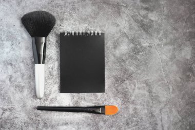 Çimento arka planında makyaj fırçaları ve siyah blok. Boşluğu kopyala, düzleştir