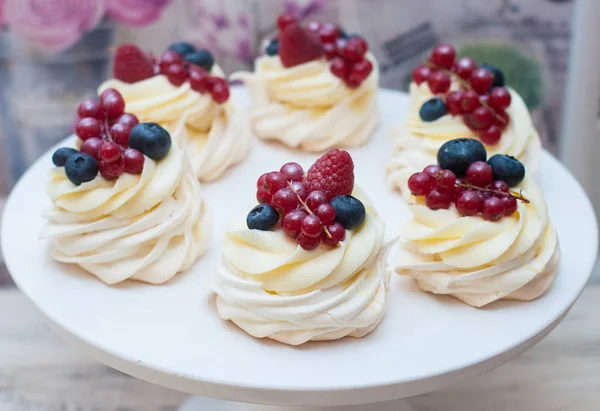 Mini pavlova cakes with cream cheese frosting and fresh berries, blueberries, raspberries and strawberries on white cake stand.