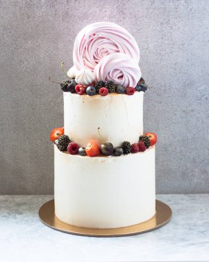 Krem peynirli zarif beyaz düğün pastası, taze çilek, yabanmersini, ahududu, gri arka planda kremalı güller.. 
