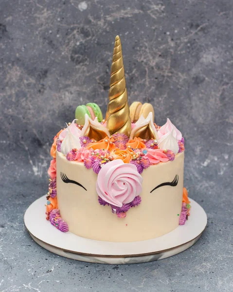 Unicorn birthday cake with golden horn and cream cheese orange, pink and purple decorations on grey background.