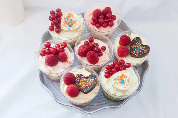 Assorted home made desserts in cups with whipped cream and fresh berries, strawberries, blueberries, raspberries, decorated with chocolate hearts.