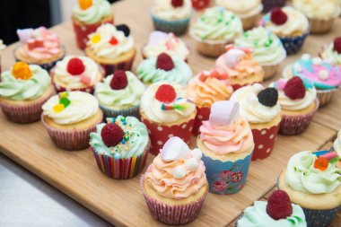 Mavi, pembe ve turuncu kremalı çeşitli renkli kekler, ahududu, şekerleme ve şekerle süslenmiş.. 