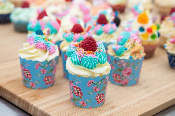 Mavi, pembe ve turuncu kremalı çeşitli renkli kekler, ahududu, şekerleme ve şekerle süslenmiş.. 