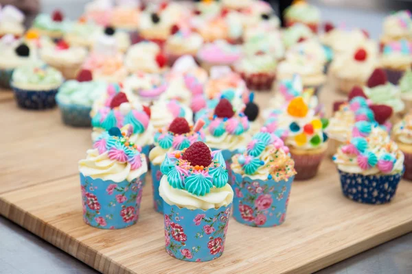 各种色彩艳丽的杯形蛋糕 带有蓝色 粉色和橙色的糖霜 装饰有覆盆子 棉花糖 洒水和糖果 — 图库照片