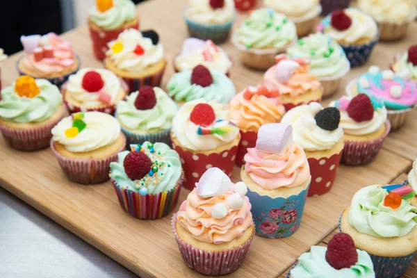 Mavi, pembe ve turuncu kremalı çeşitli renkli kekler, ahududu, şekerleme ve şekerle süslenmiş.. 