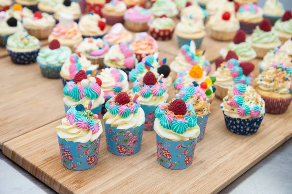 Assorted colorful cupcakes with blue, pink and orange frosting, decorated with raspberries, marshmallow, sprinkles and candies.