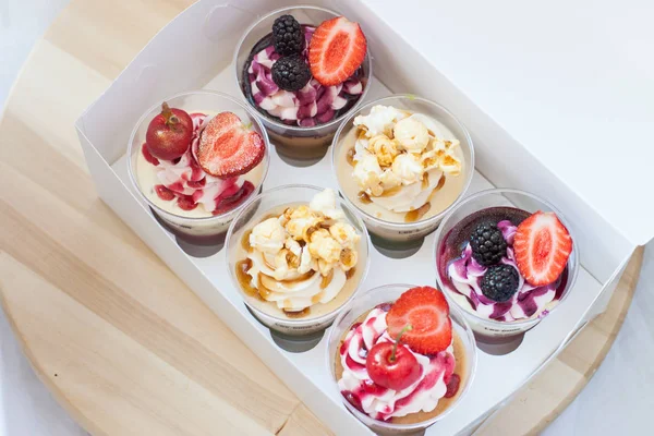 Mousse desserts in cup with cream cheese frosting, berry sauce, salted caramel, strawberry, cherry, raspberry and popcorn.