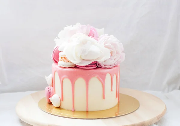 White cake with pink melted chocolate, fresh roses and peonies, macaroons and meringues.