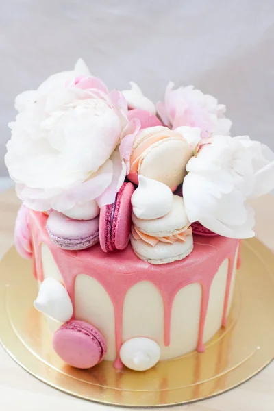 White cake with pink melted chocolate, fresh roses and peonies, macaroons and meringues.