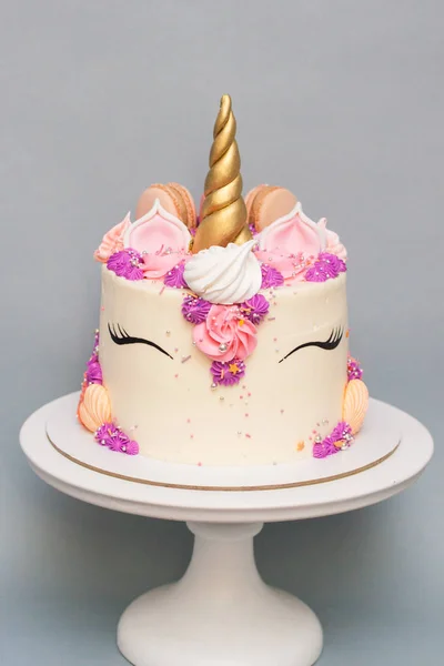 Unicorn cake with golden horn, pink, violet and peach cream cheese decoration on grey background