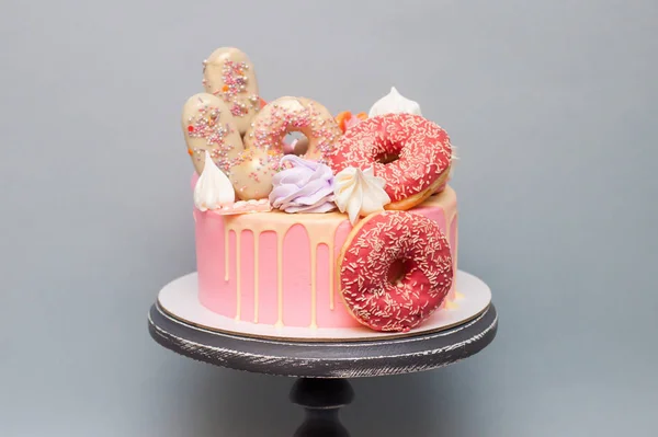 Pink cake with glazed donuts, cake pops,meringues, candies, melted chocolate and macaroons.