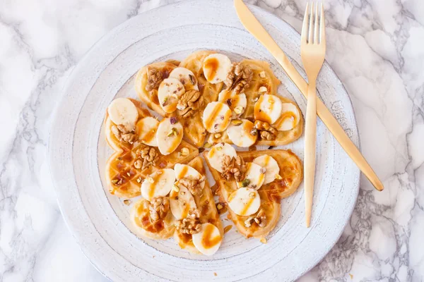 Heart shaped waffles with salted caramel sauce, fresh bananas, pecan nuts and pumpkin seeds.