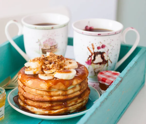 Fluffy pancakes with corn syrup, bananas and pecan nuts in turquoise tray.