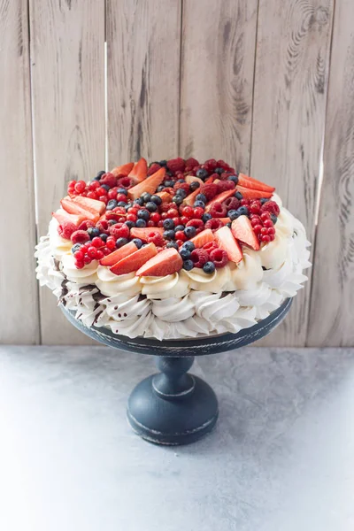 Meringue pavlova cake decorated with fresh berries, strawberries, raspberries, blueberries and red currant.