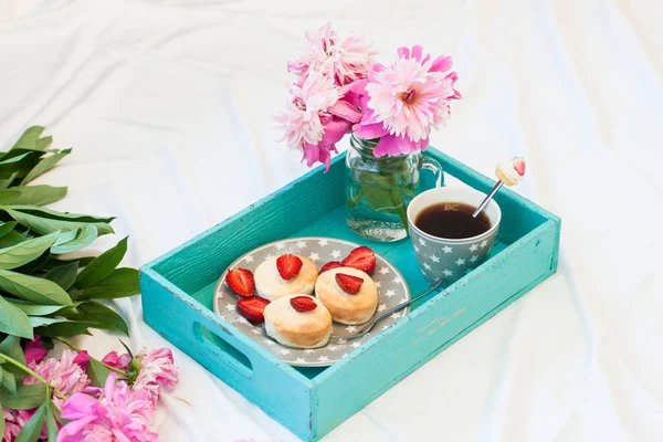 Breakfast in bed with cottage cheese pancakes, fresh strawberries, peonies and cup of coffee.