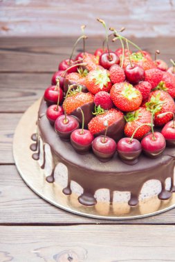 Erimiş çikolatalı cheesecake, taze çilek, kiraz ve ahududu ahşap arka planda.. 