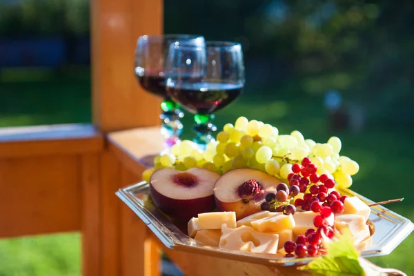 Cheese board with cutted peaches, green grape, berries, apples and two glasses of red wine