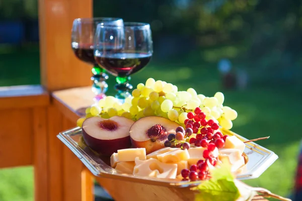 Cheese board with cutted peaches, green grape, berries, apples and two glasses of red wine