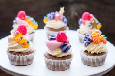 Chocolate cupcakes with multi colored frosting, bright pink, orange and purple swirls, candies, jelly and golden stars. 