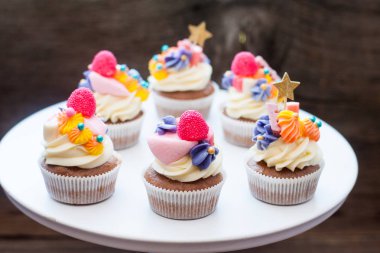 Chocolate cupcakes with multi colored frosting, bright pink, orange and purple swirls, candies, jelly and golden stars. 