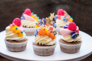 Chocolate cupcakes with multi colored frosting, bright pink, orange and purple swirls, candies, jelly and golden stars. 