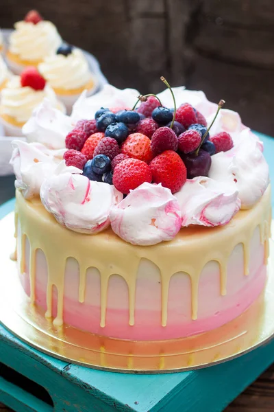 Pink and ivory cake with melted chocolate, meringue clouds and hanful of strawberries, raspberries, cherries and blueberries.