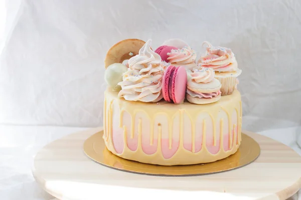 Tender pink and ivory cake with melted white chocolate, macaroons, donuts, cupcake and meringue decoration.