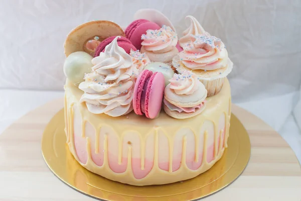Tender pink and ivory cake with melted white chocolate, macaroons, donuts, cupcake and meringue decoration.