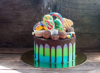 Green and blue birthday cake with melted chocolate, cupcake, cake pops, candies, lollipops, waffles and sprinkles. 