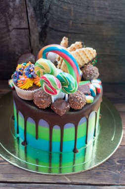 Green and blue birthday cake with melted chocolate, cupcake, cake pops, candies, lollipops, waffles and sprinkles. 