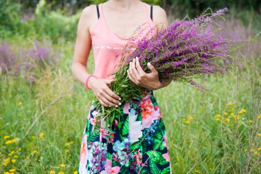 Young woman in the field holding a bunch with wild lilac, purple and vilet flowers. 