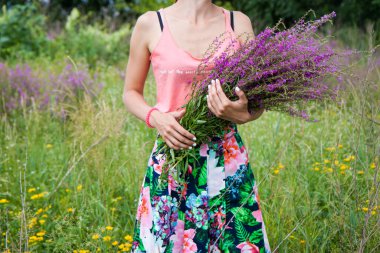 Young woman in the field holding a bunch with wild lilac, purple and vilet flowers. 