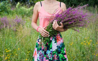 Young woman in the field holding a bunch with wild lilac, purple and vilet flowers. 