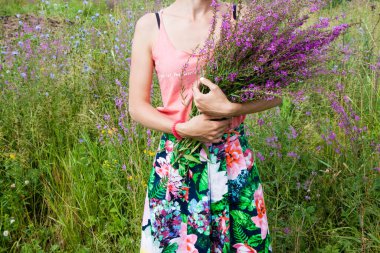 Young woman in the field holding a bunch with wild lilac, purple and vilet flowers. 