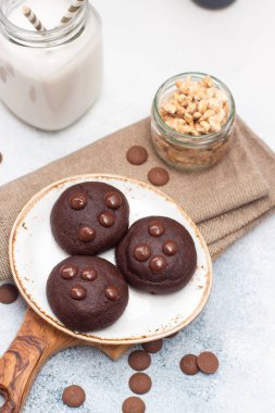 Çikolatalı kurabiyeler beyaz tabakta çikolata damlaları ve gri arka planda bir bardak süt.