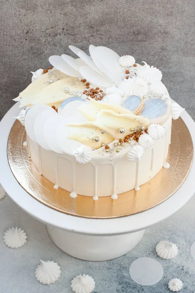 Elegant white cake decorated with melted white chocolate, meringues, waffle paper and macaroons.