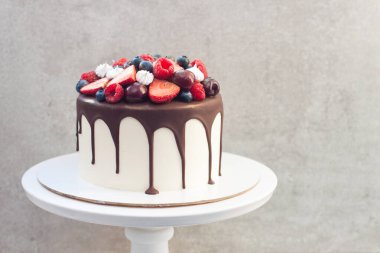 Erimiş siyah çikolatalı beyaz pasta, taze çilek, yabanmersini, ahududu ve gri arka planda kiraz.