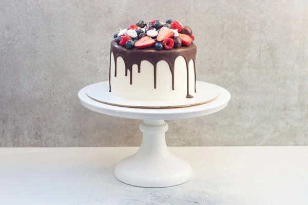 Erimiş siyah çikolatalı beyaz pasta, taze çilek, yabanmersini, ahududu ve gri arka planda kiraz.