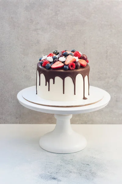 White cake with melted dark chocolate, fresh strawberries, blueberries, raspberries and cherries on gray background