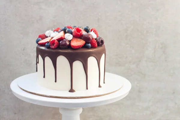 White cake with melted dark chocolate, fresh strawberries, blueberries, raspberries and cherries on gray background